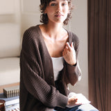 Modal sitting in a living room wearing Chunky Knit Women's Waffle Cardigan in Espresso over white camisole and blue jeans