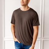 Man wearing Men's Crew Neck Tee in Espresso and blue jeans in front of a white wall