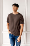 Man wearing Men's Crew Neck Tee in Espresso and blue jeans in front of a white wall