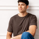 Man sitting in front of a white wall wearing Men's Crew Neck Tee in Espresso and blue jeans