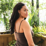 Woman in a brown dress standing outdoors with greenery in the background