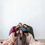 Models sitting together wrapped in Quilted Blankets 2.5 in Burgundy, Atlantic, Fir, Latte, Espresso and Bisque