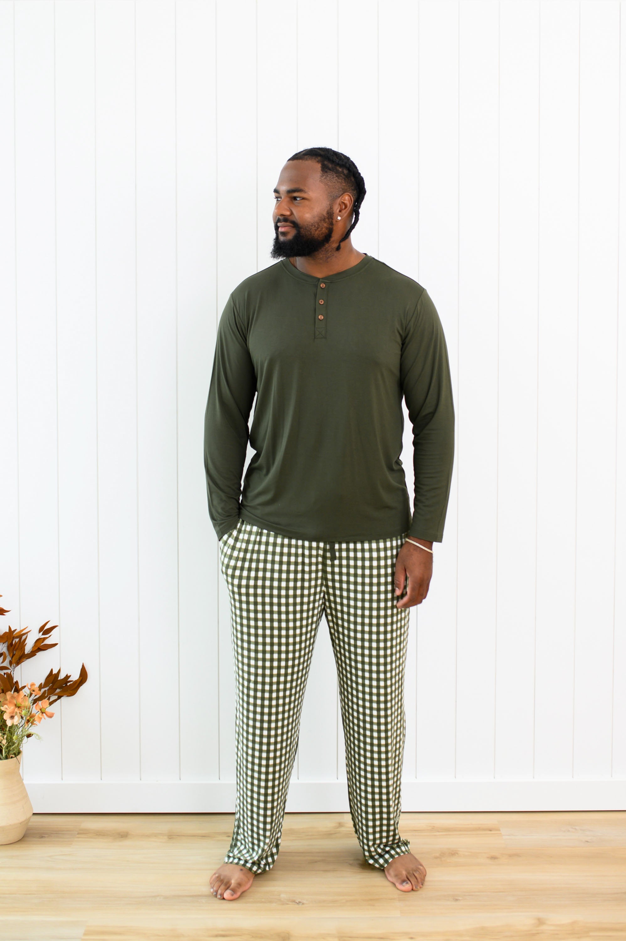 Model standing in front of a white paneled wall in the Men's Lounge Pants in Gingham Fir and Fir Henley 