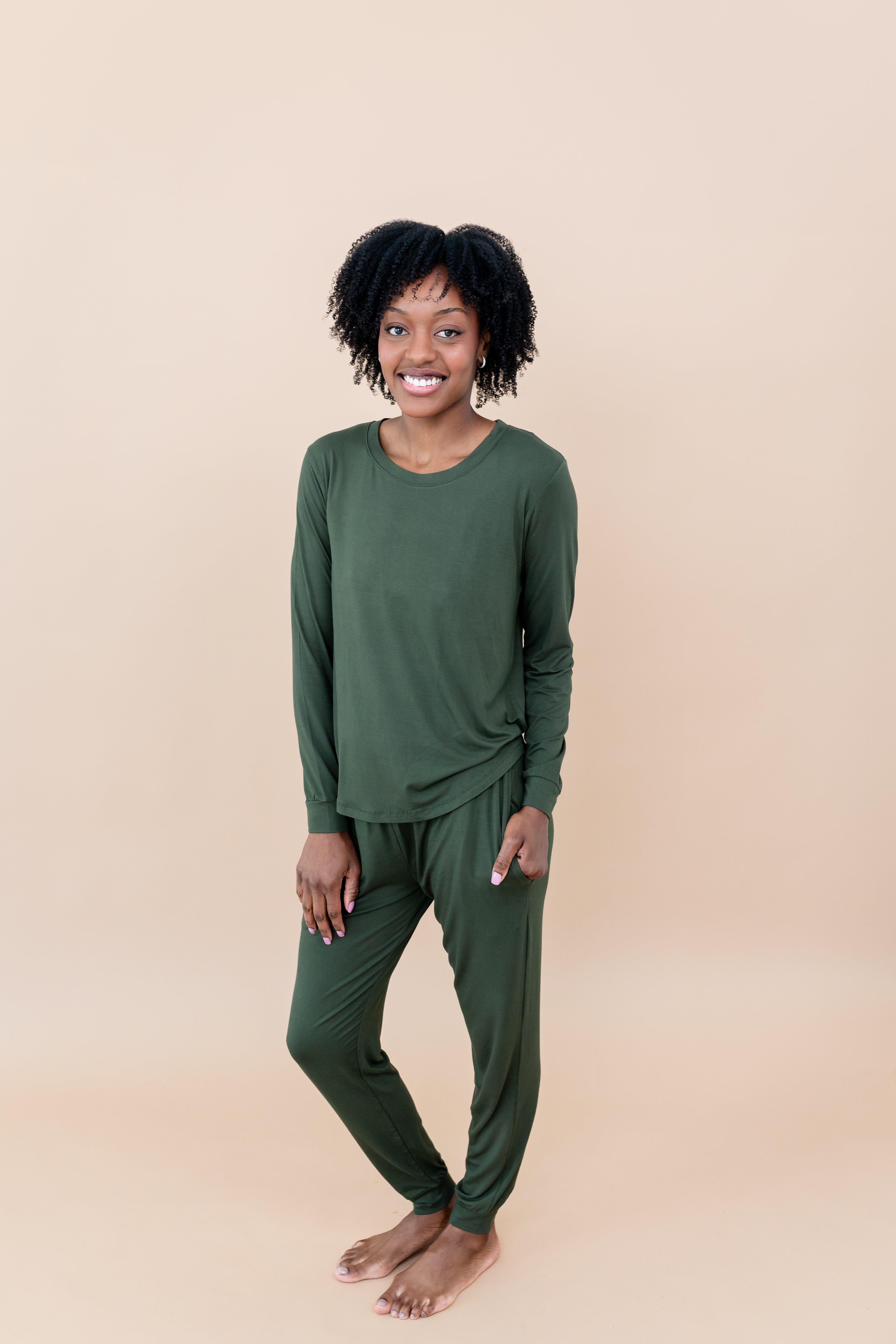Model in a tan room wearing the Smiling model in grassy field wearing the Kyte Women's Jogger Set in Fir
