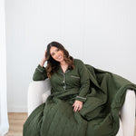 Smiling model with head tilted while wrapped in Bamboo Quilt Blanket in Fir 2.5