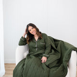 Smiling model with head tilted while wrapped in Bamboo Quilt Blanket in Fir 2.5