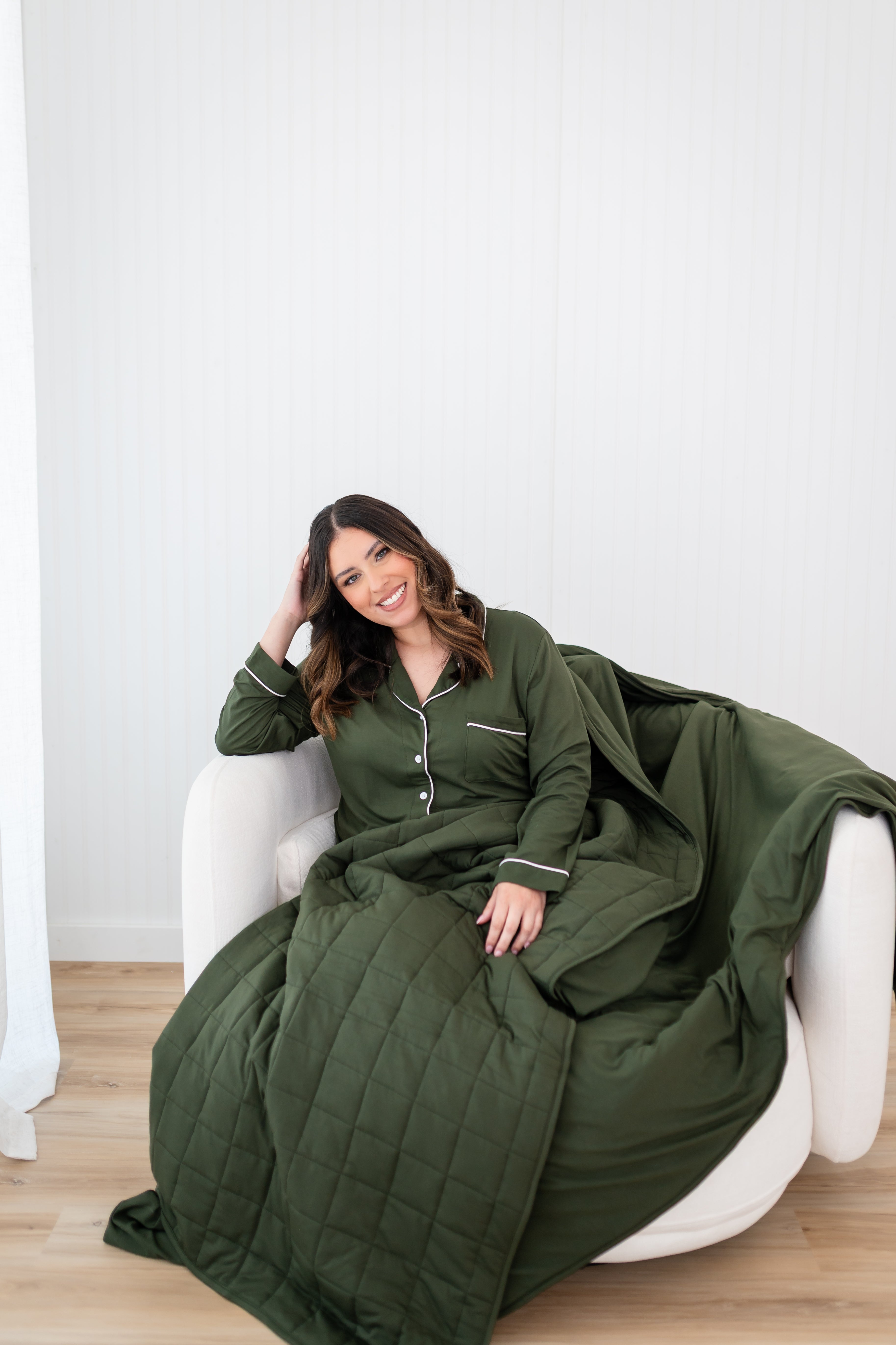 Smiling model with head tilted while wrapped in Bamboo Quilt Blanket in Fir 2.5