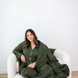 Model sitting on a white couch sofa wrapped in a the bamboo Quilt Blanket in Fir 2.5 and wearing the matching Long Sleeve Pajama Set