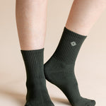 A close-up of a person's legs wearing dark forest green ribbed crew socks against a solid beige background.