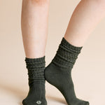 A close-up of a person's legs wearing dark olive green ribbed crew socks against a solid beige background.