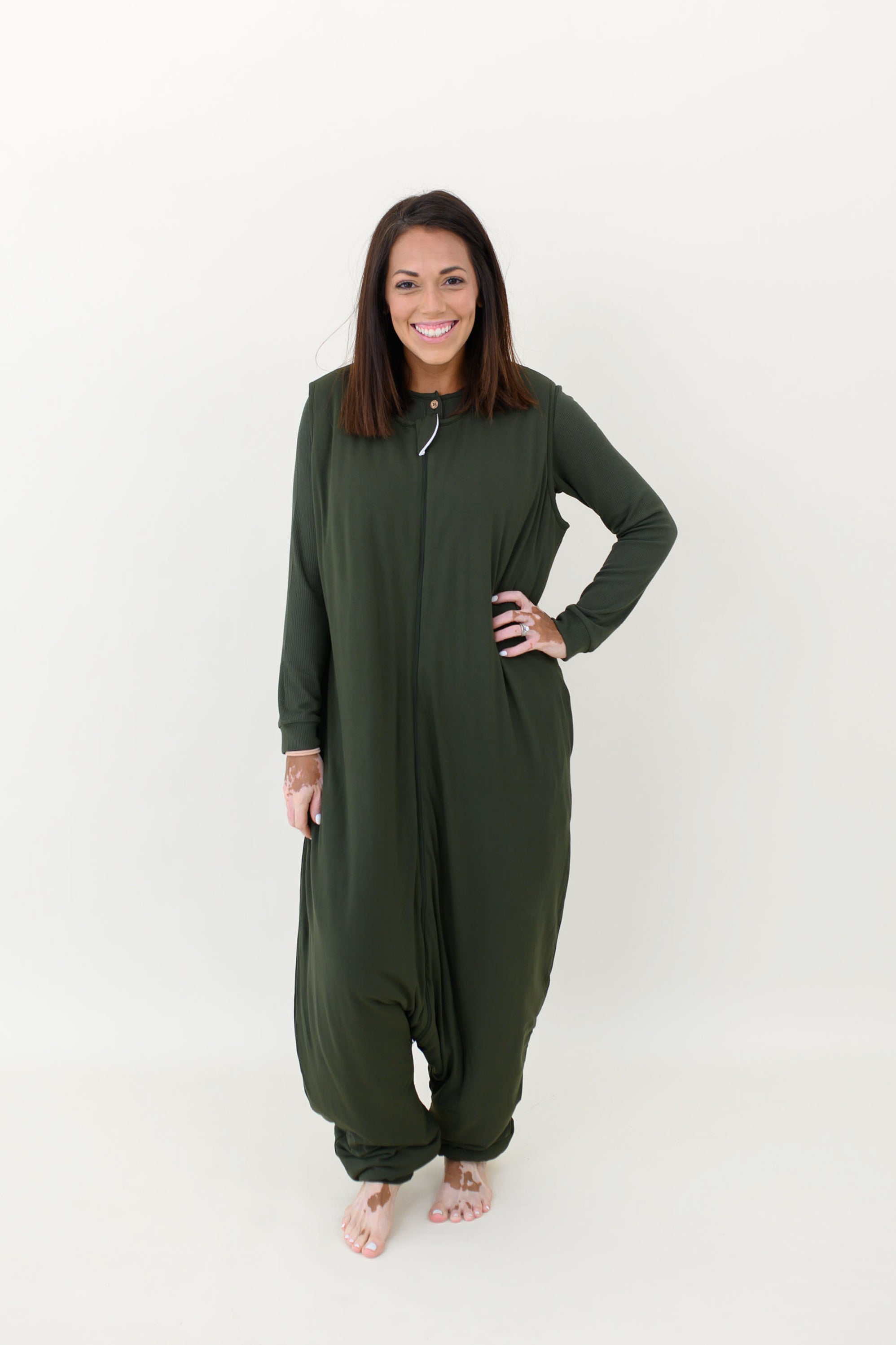 Smiling model wearing the Kyte Adult Sleep Bag Walker in Fir with hand on hip and matching top beneath it