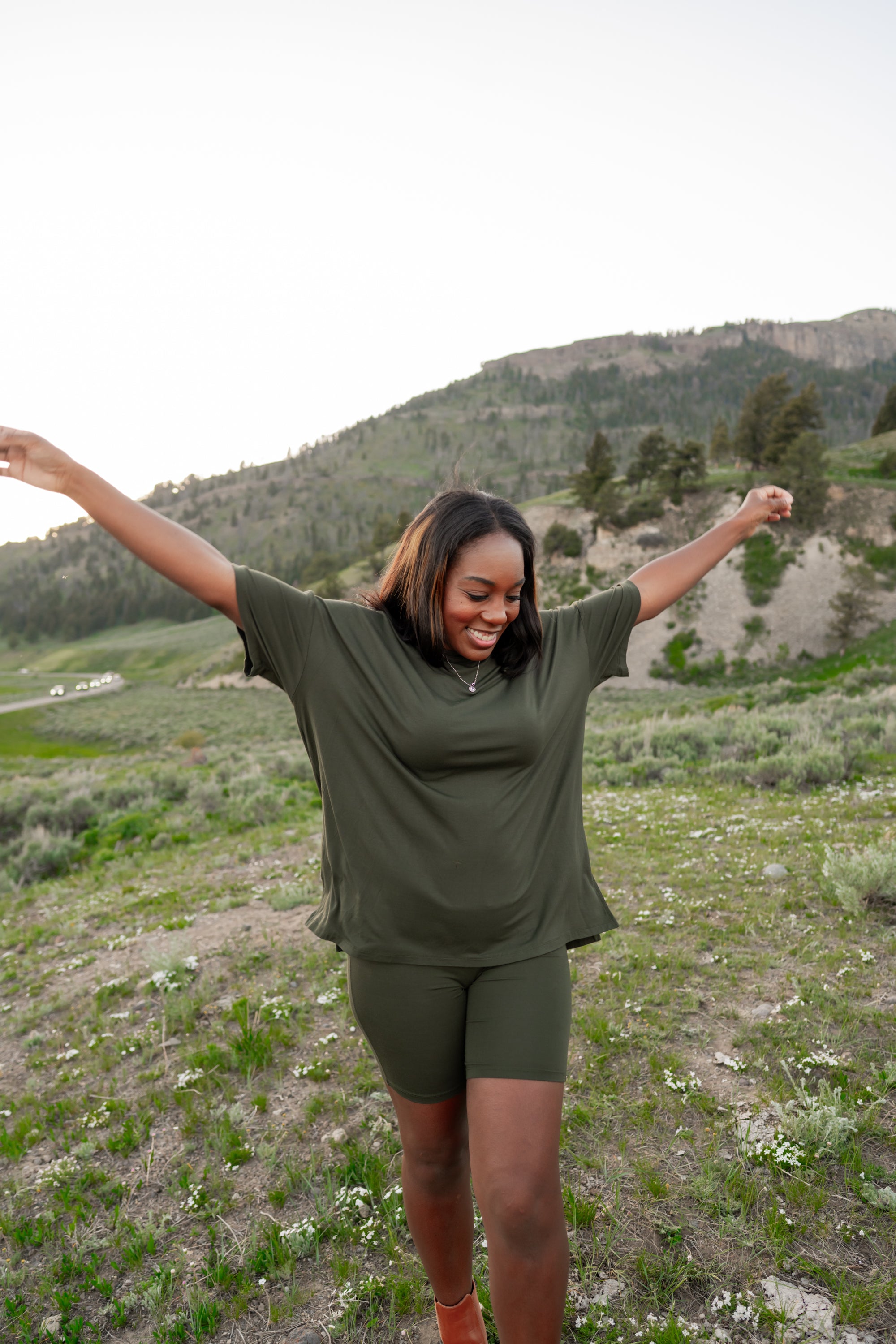 Model with arms spread out while wearing the Kyte Women's Biker Short Set in Fir in front of mountains