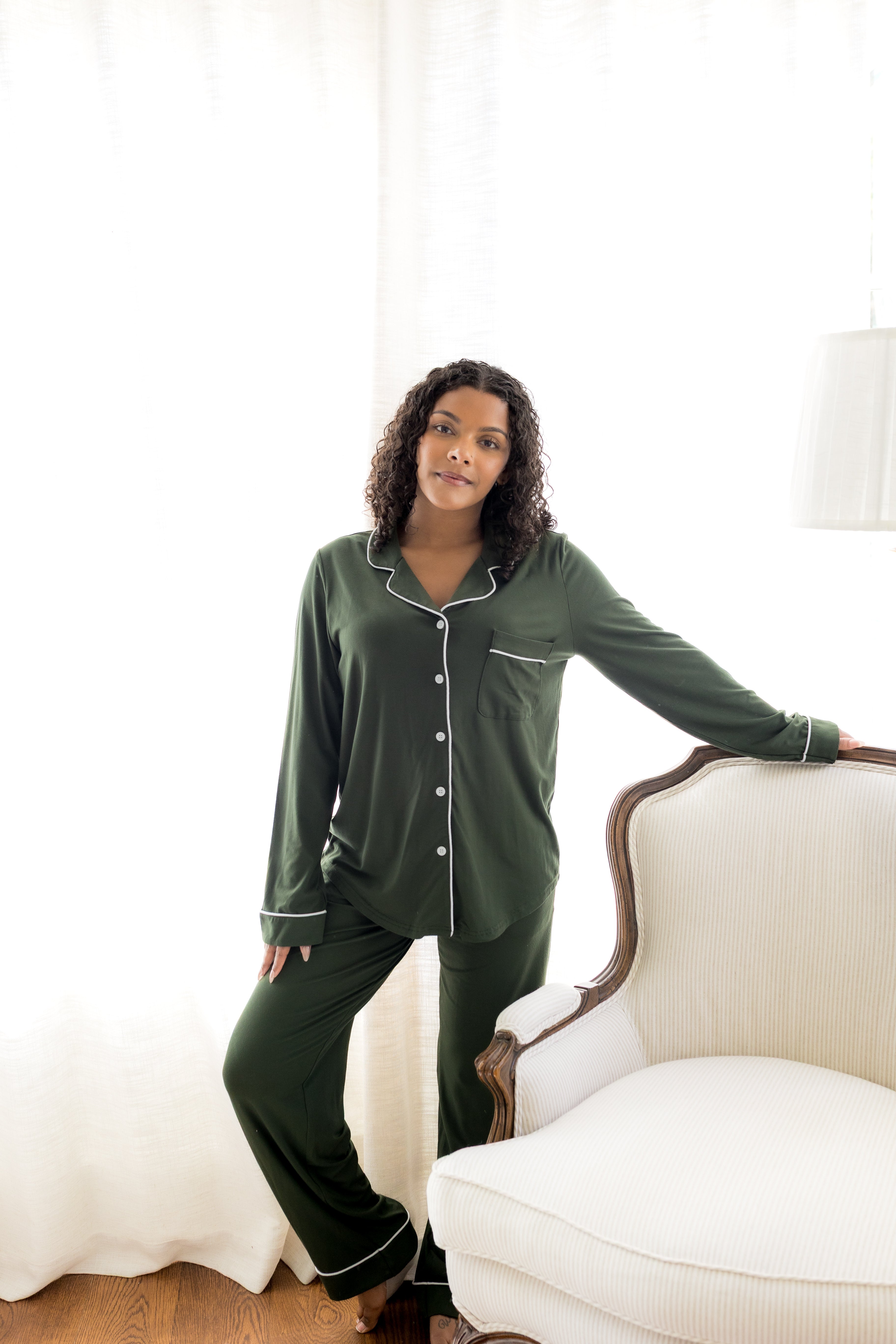 Woman wearing green pajamas sitting on a white chair in a bright room.