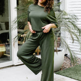 Female standing on a concrete patio in front of glass windows on a white brick house wearing the Women's Wide Leg Pant in Fir with matching short sleeve tee