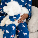 Woman in blue pajamas that have winter animals on them holding a dog with matching printed bandana 