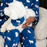 Woman in blue pajamas that have winter animals on them holding a dog with matching printed bandana 