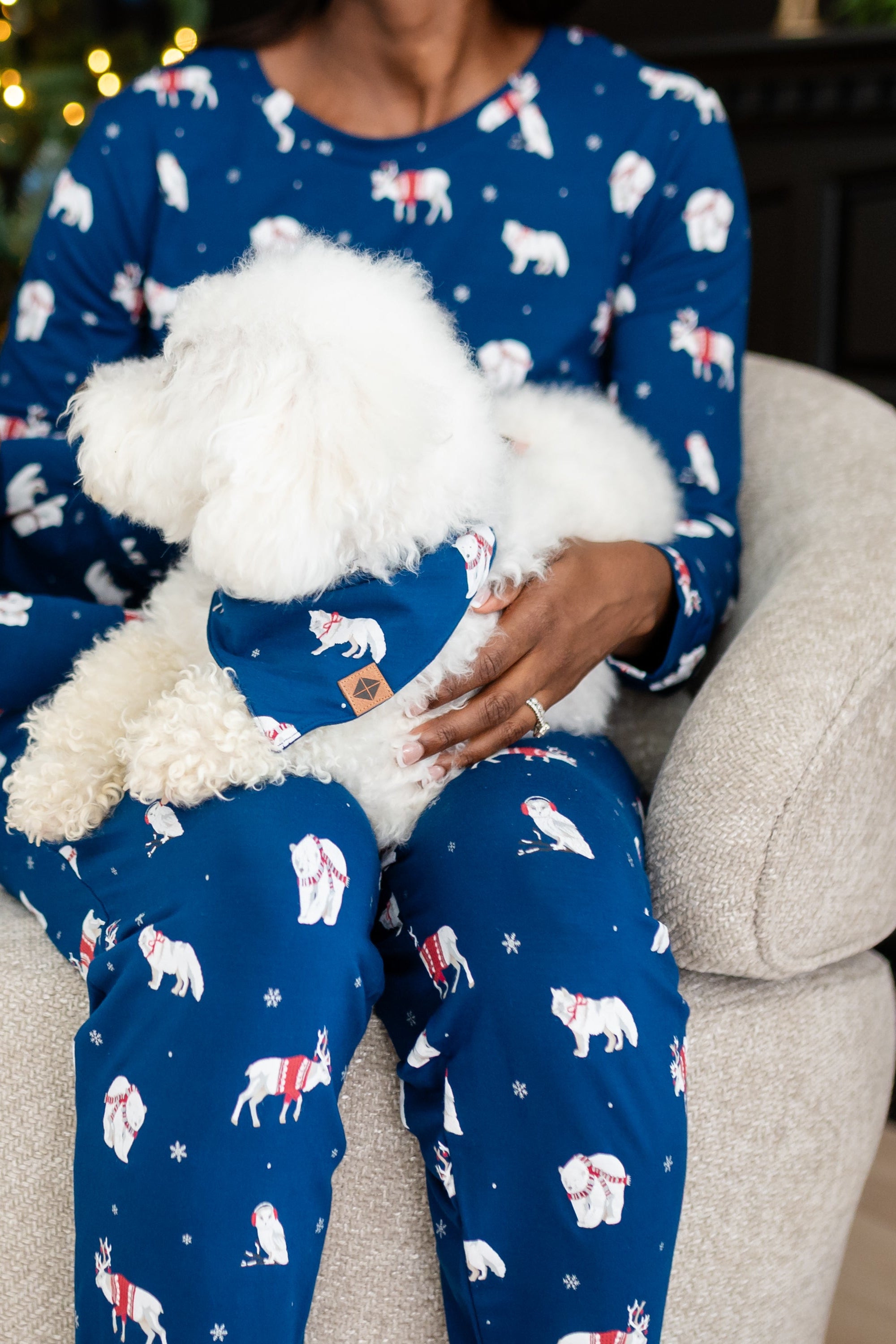 Woman in blue pajamas that have winter animals on them holding a dog with matching printed bandana 