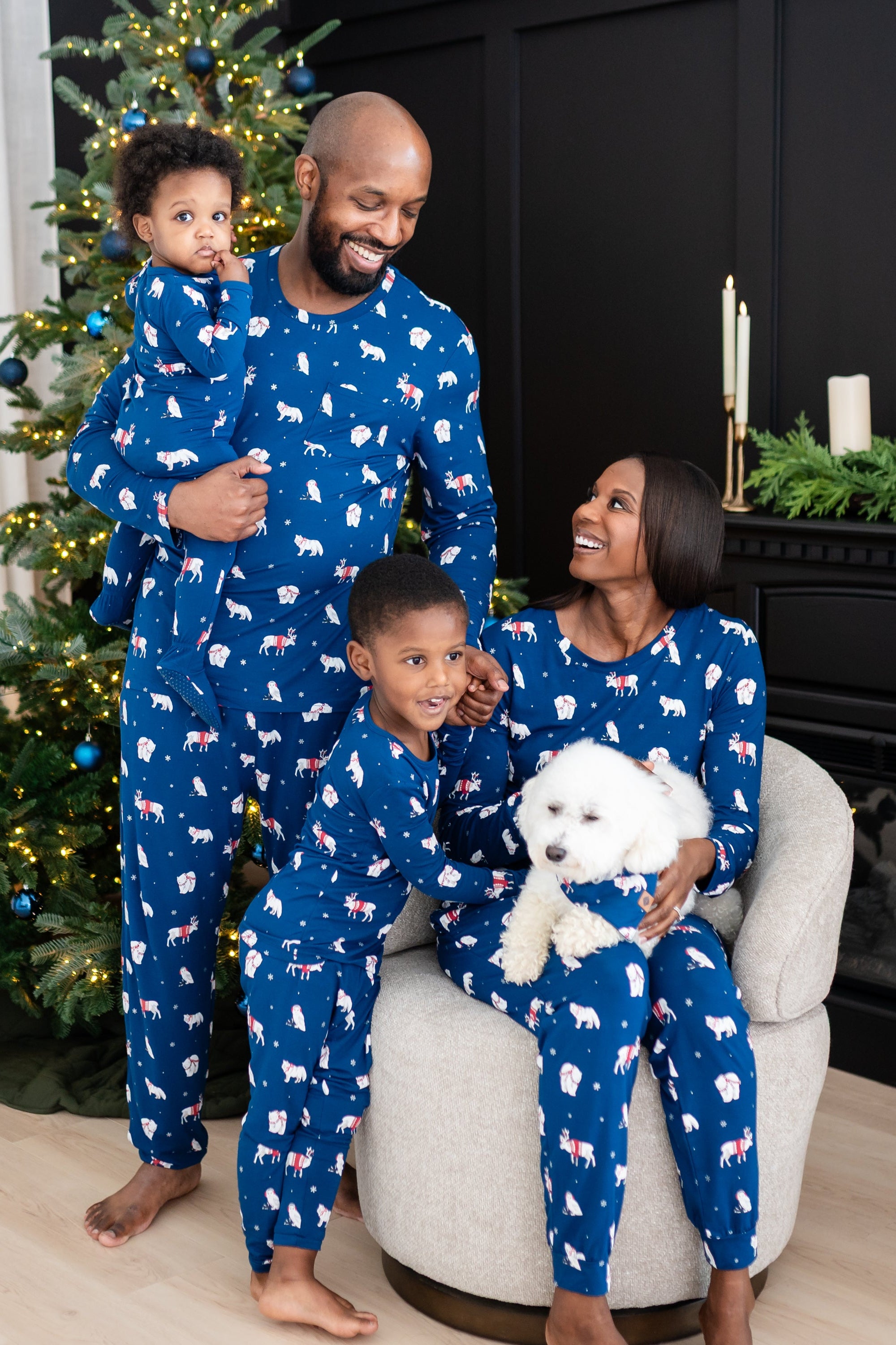 Family of 4 and dog all wearing matching holiday pajamas that are blue with a winter forest animal print
