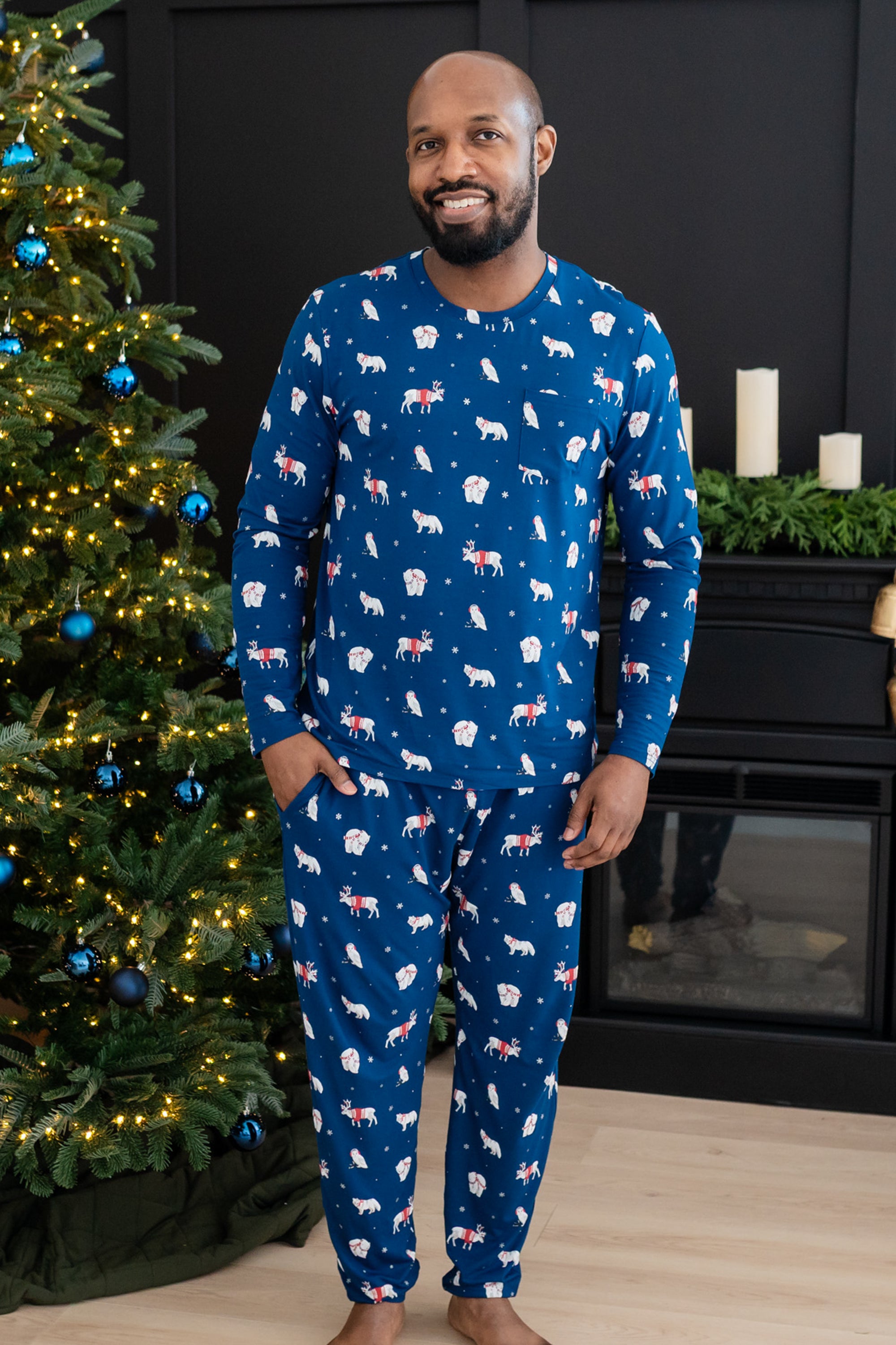 Male modeling blue pajama set with white forest animals print standing in front of a christmas tree 