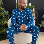 Male model sitting on a cushioned chair wearing the Men's Jogger Set in Frosty Friends in front of two decorated Christmas trees and a black fireplace