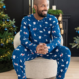 Male model sitting on a cushioned chair wearing the Men's Jogger Set in Frosty Friends in front of two decorated Christmas trees and a black fireplace
