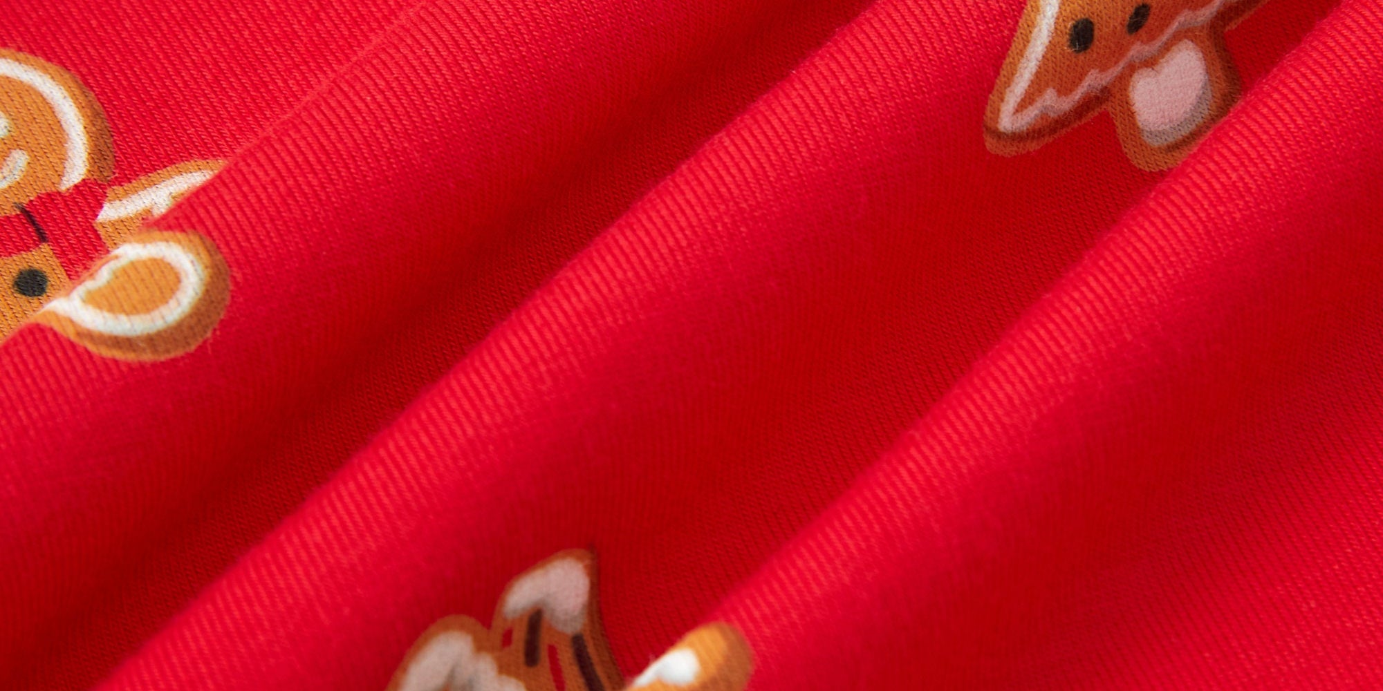 A close-up of bright red fabric with repeating gingerbread house and tree motifs in orange, white, and brown.
---1605 1