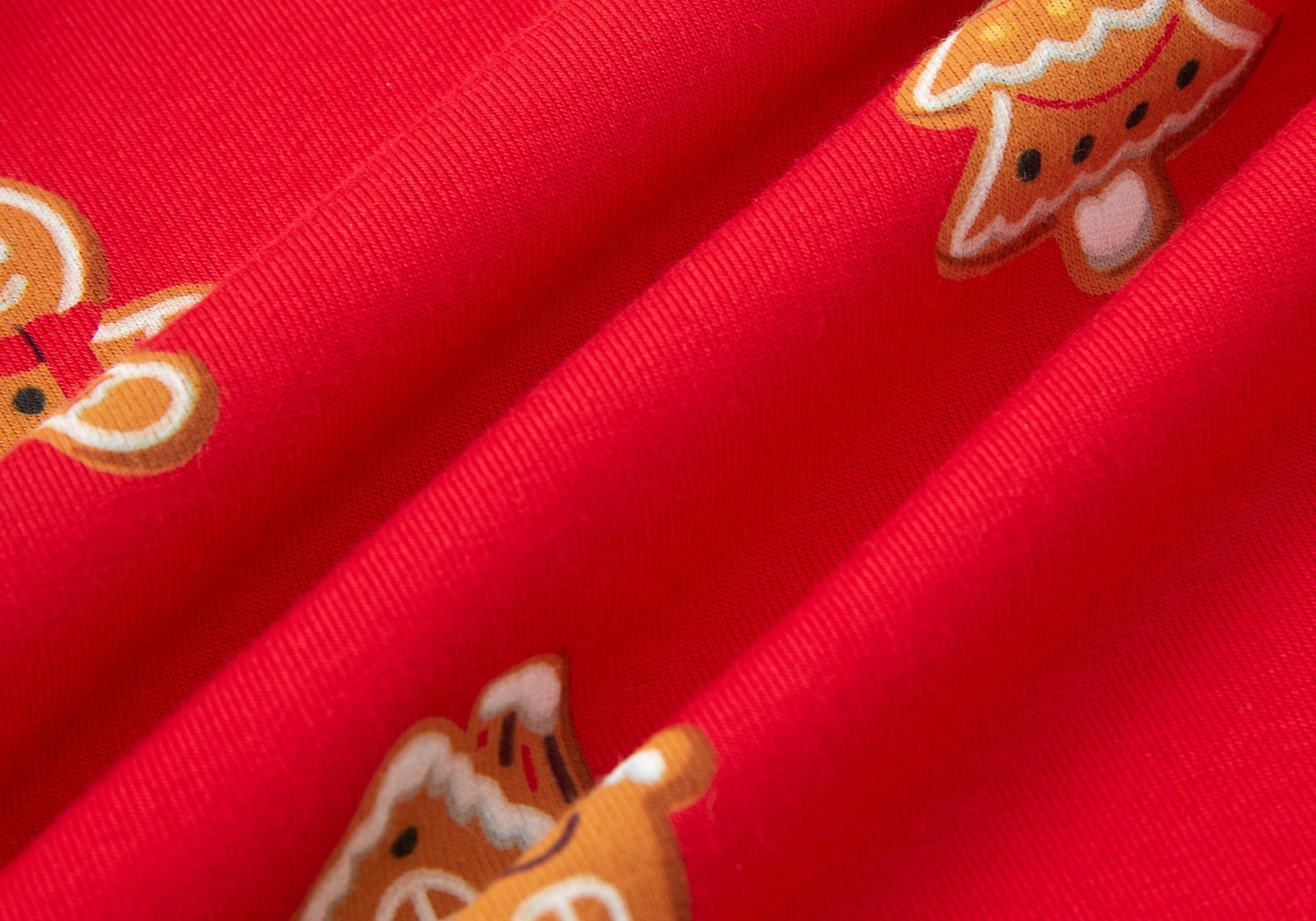A close-up of bright red fabric with repeating gingerbread house and tree motifs in orange, white, and brown.
---1605 1