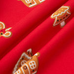 A close-up of bright red fabric with repeating gingerbread house and tree motifs in orange, white, and brown.