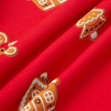 A close-up of bright red fabric with repeating gingerbread house and tree motifs in orange, white, and brown.