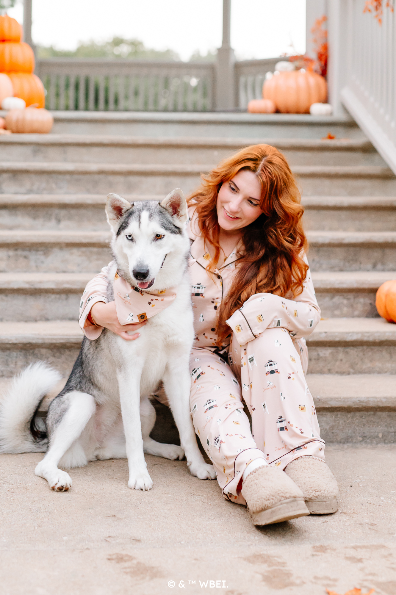 Female model sitting at the bottom of concrete steps wearing the Long-Sleeved Women's Pajama Set in Gilmore Girls with her arm around a husky 