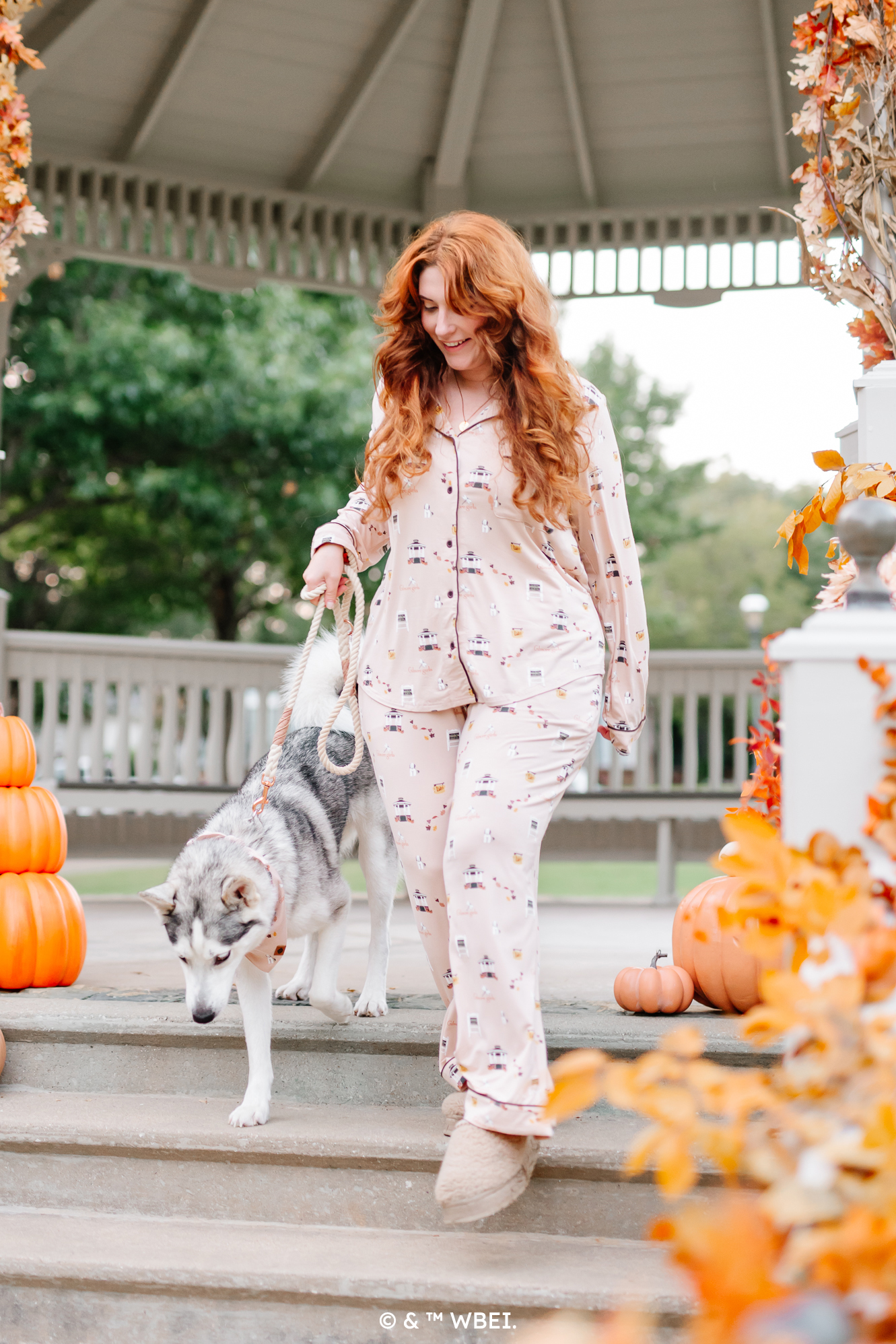 Female model wearing the Long-Sleeved Women's Pajama Set in Gilmore Girls walking her dog down the steps of a gazebo