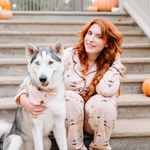 Female model sitting on concrete steps wearing the Long-Sleeved Women's Pajama Set in Gilmore Girls with her arm around a husk dog wearing a matching dog bandana