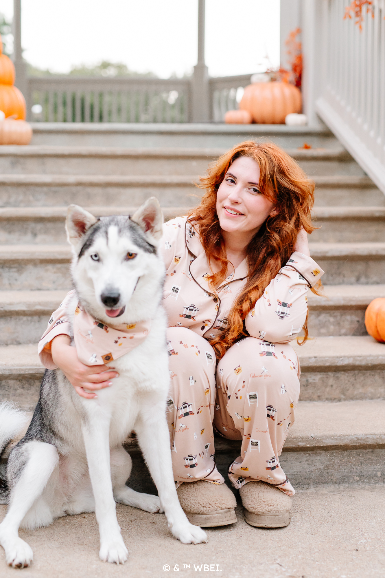 Female model sitting on concrete steps wearing the Long-Sleeved Women's Pajama Set in Gilmore Girls with her arm around a husk dog wearing a matching dog bandana