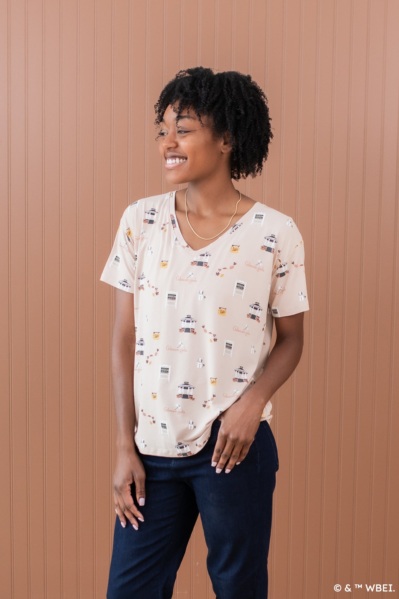Smiling model looking to the side and wearing the Women's Relaxed Fit V-Neck in Gilmore Girls paired with dark jeans