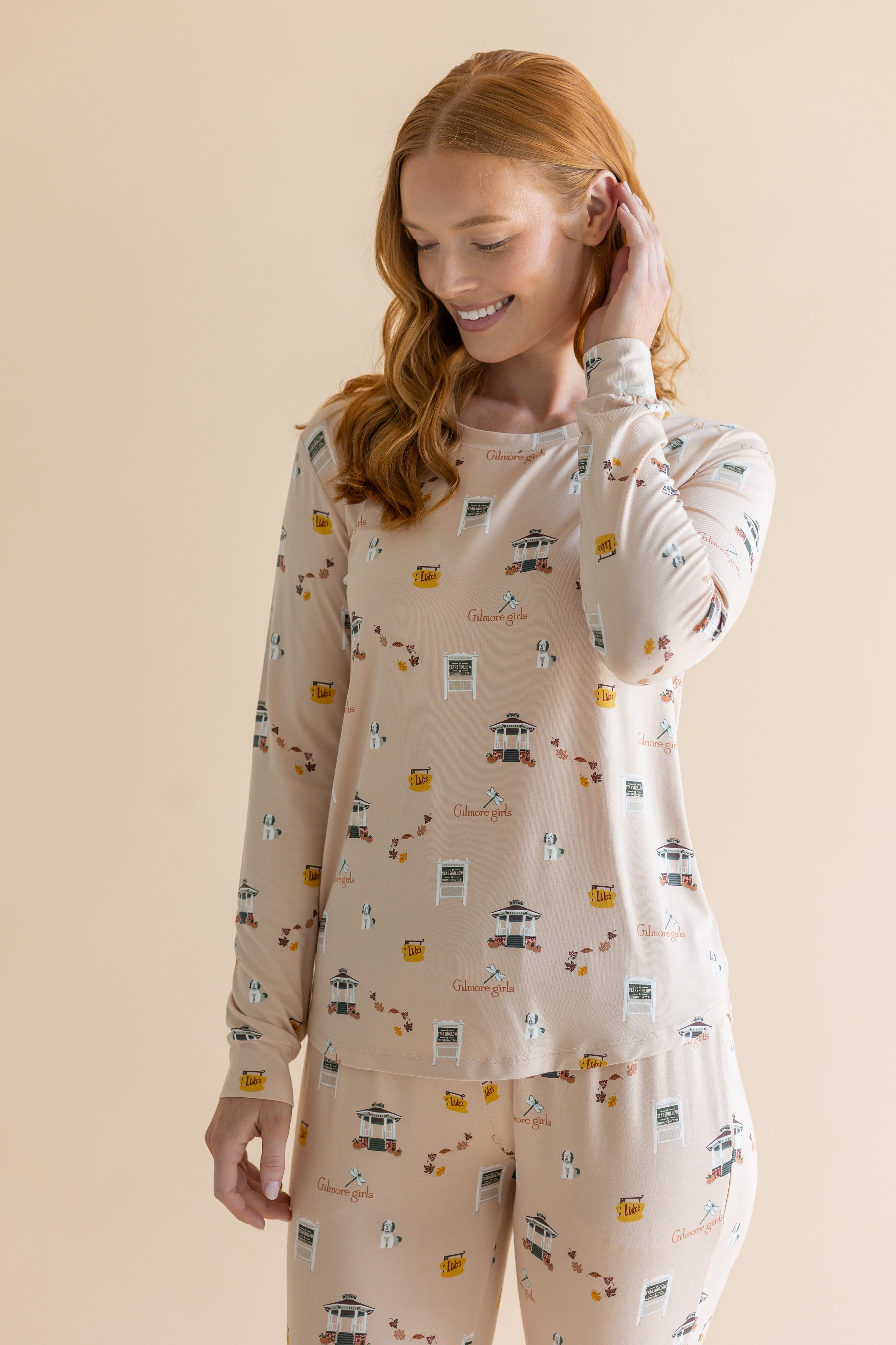 Close up of the top from the Women's Jogger Pajama Set in Gilmore Girls on model who is smiling downwards with one hand in her hair 