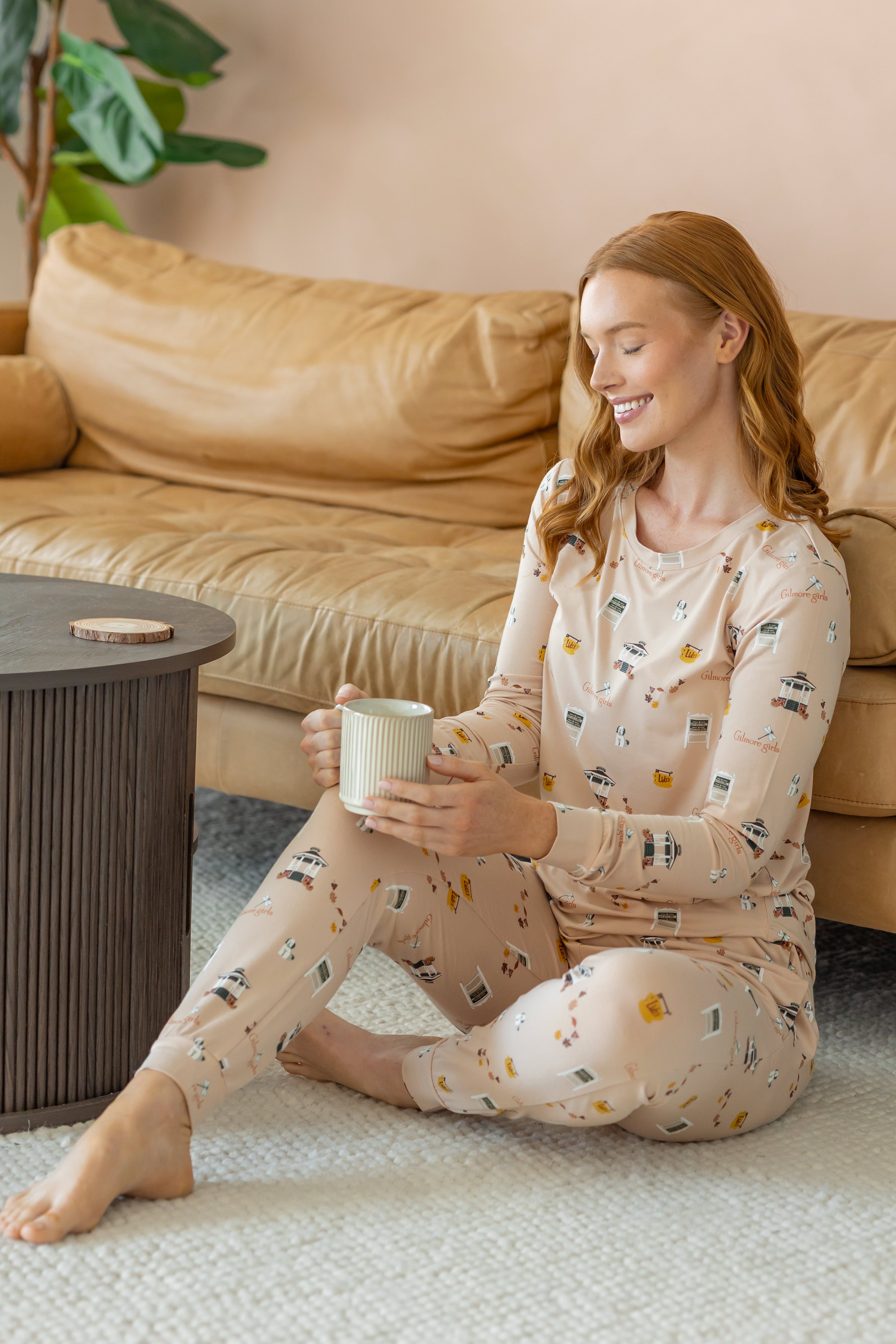 Woman sitting on the floor leaning on a camel leather couch while wearing the Women's Jogger Pajama Set in Gilmore Girls and holding a coffee mug