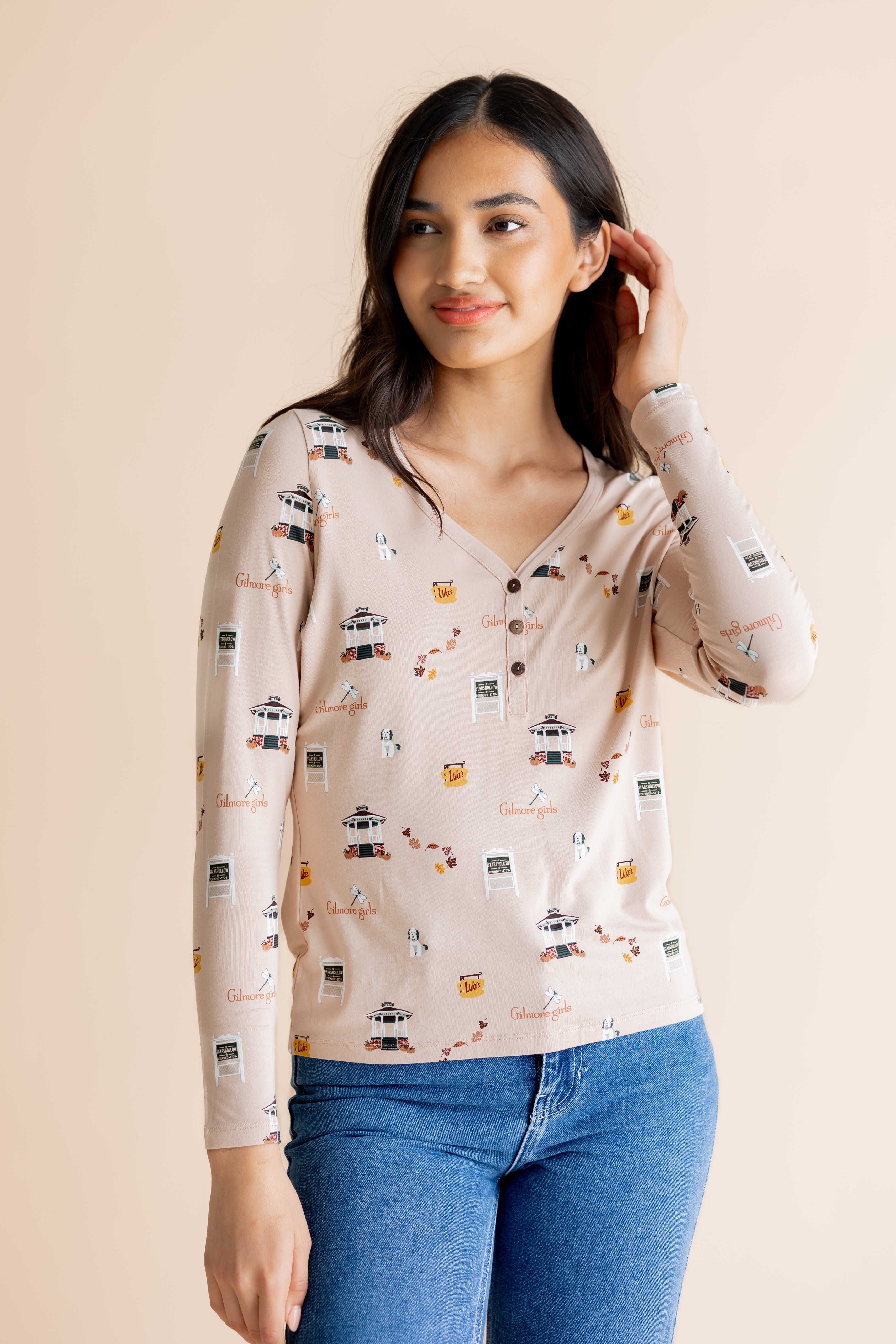 Model looking to the side in front of a beige background while wearing the Women's Long Sleeve Henley Tee in Gilmore Girls paired with medium wash denim jeans