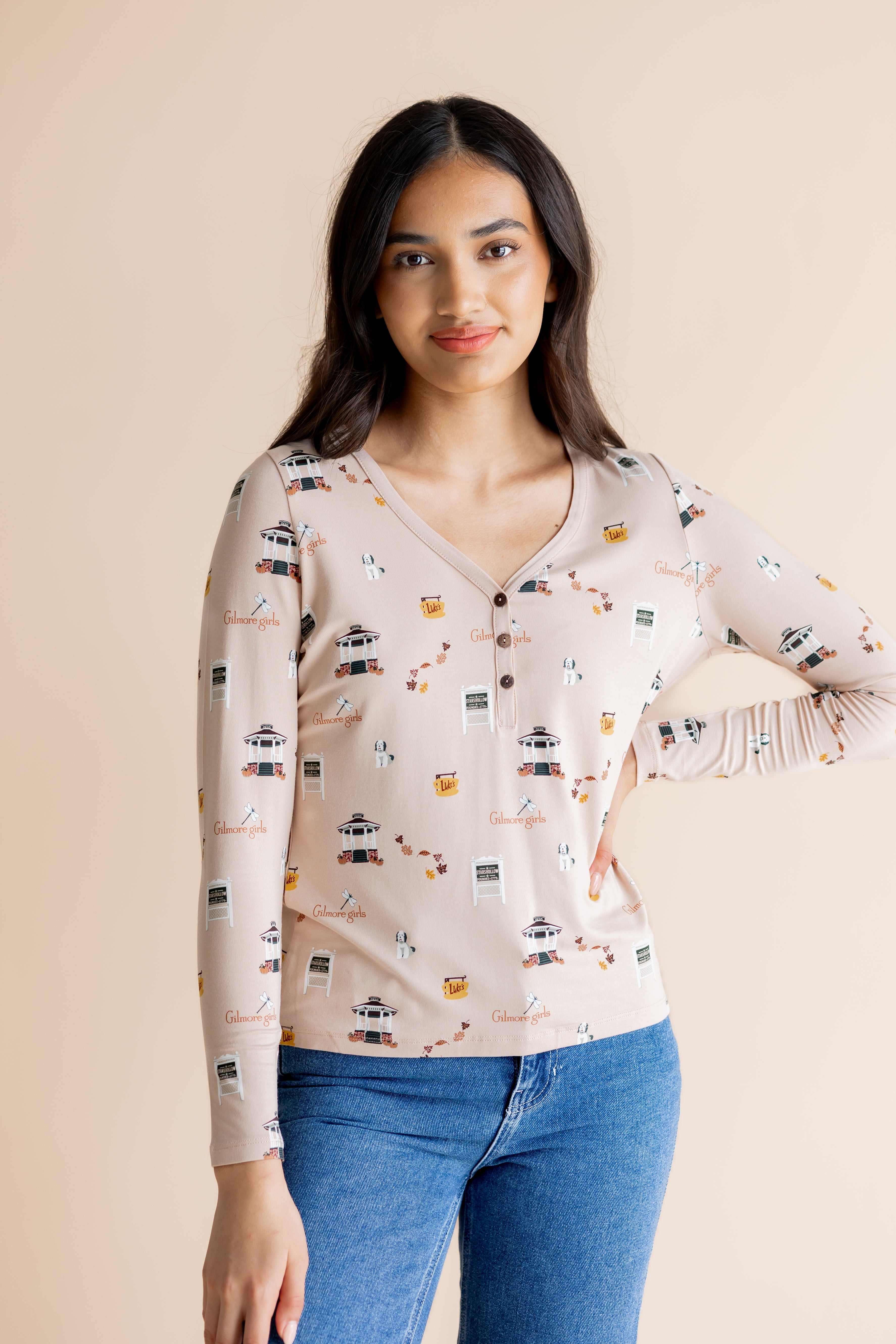 Model with hand on her hip wearing the Women's Long Sleeve Henley Tee in Gilmore Girls while standing in front of a beige background 