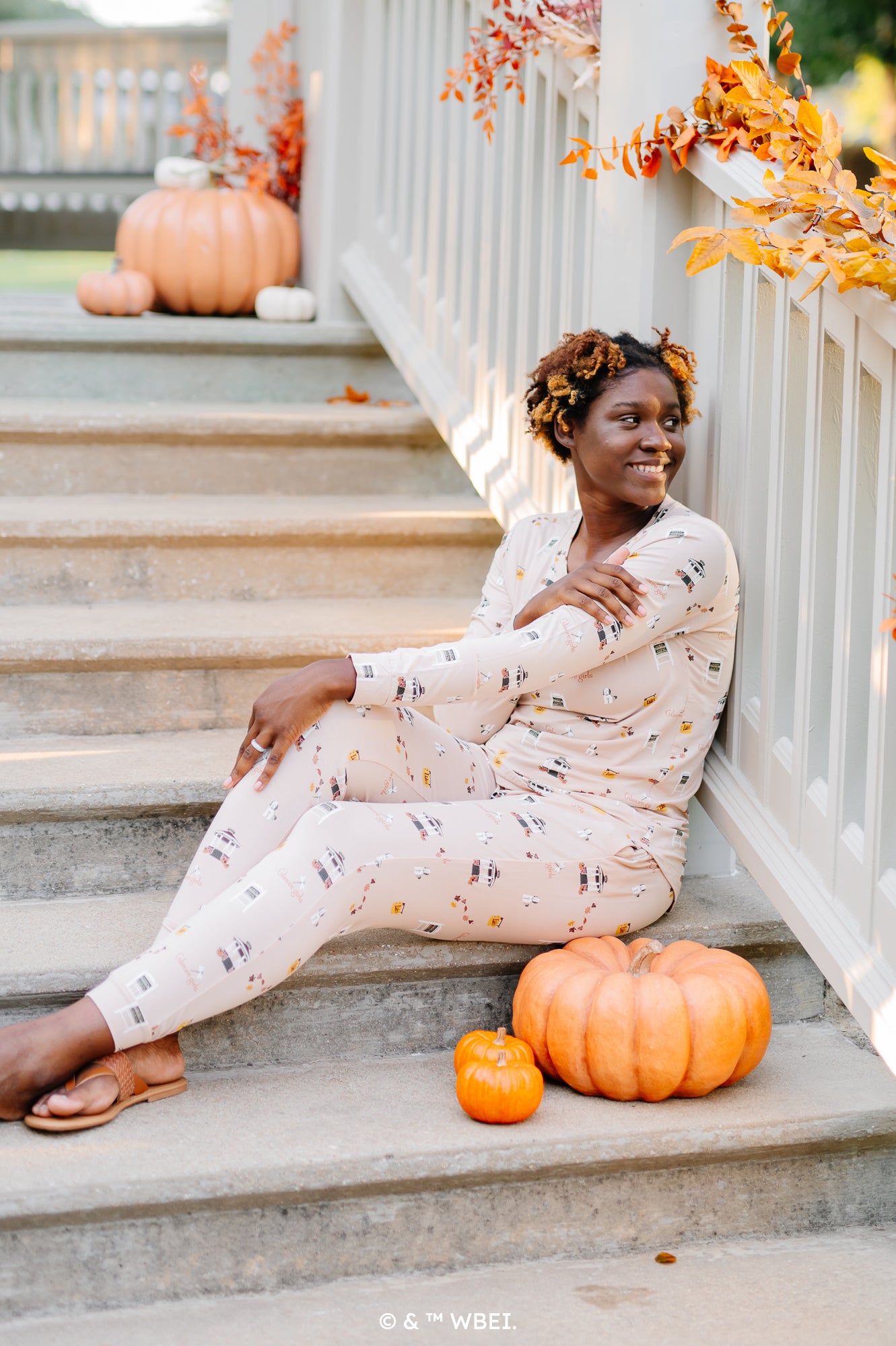 Woman sitting on concrete stairs next to a pumpkin while modeling the Women's Jogger Pajama Set in Gilmore Girls