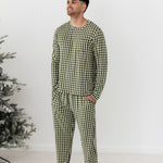 Man wearing green checkered pajamas standing in front of a white wall with a Christmas tree.