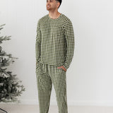 Man wearing green checkered pajamas standing in front of a white wall with a Christmas tree.