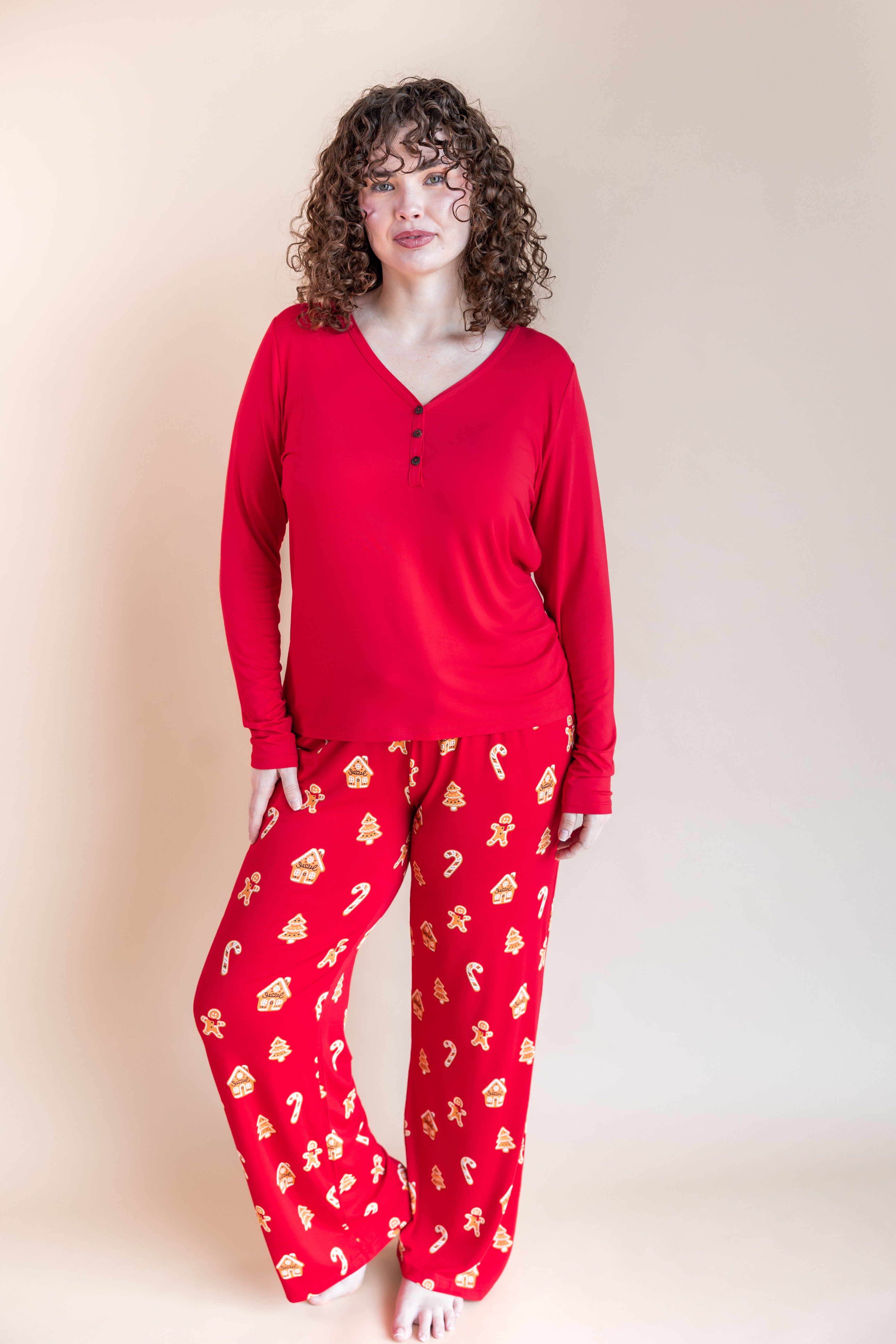 Woman soft smiling with her heel propped on her other foot wearing gingerbread lounge pants and long sleeve pajama tee in cardinal