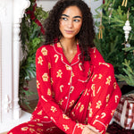 Woman sitting with one leg bent in with the other propped up looking over to the side in long sleeve pajama set in gingerbread print

---PJ 