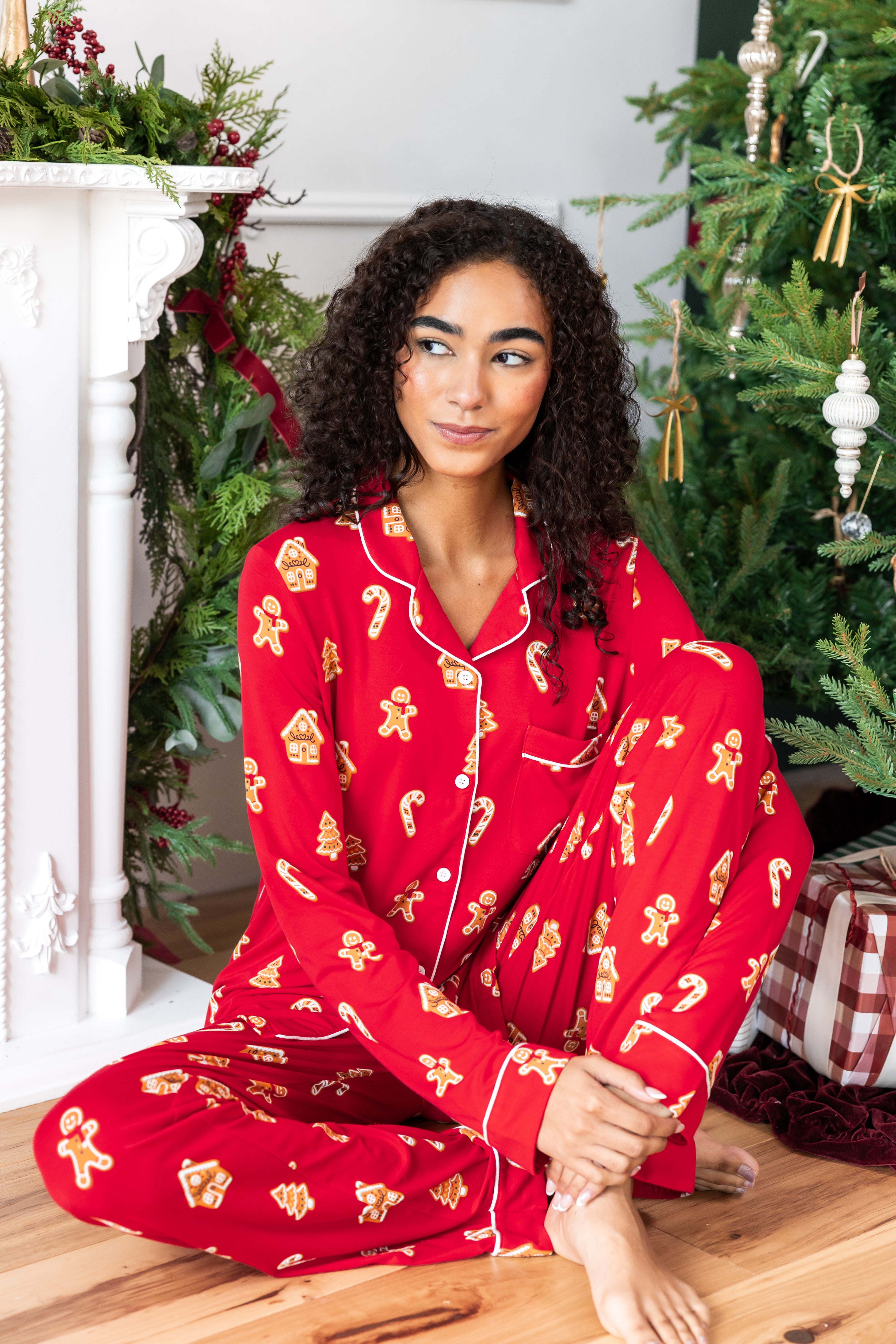 Woman sitting with one leg bent in with the other propped up looking over to the side in long sleeve pajama set in gingerbread print

---PJ 