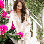 Woman looking down at flowers while modeling the Kyte Women's Long Sleeve Pajama in Bisque Gingham