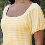 Woman wearing a yellow checkered dress with a blurred green background