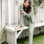 Model sitting on a white bench while wearing the Women's Long Sleeve Pajama Set in Gingham Fir