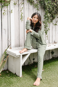Model sitting on a white bench while wearing the Women's Long Sleeve Pajama Set in Gingham Fir