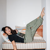 Model laying in a book nook while wearing the Women's Lounge Pants in Gingham Fir