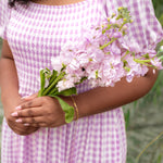 Person wearing a purple checkered dress holding pink flowers with a blurred green background